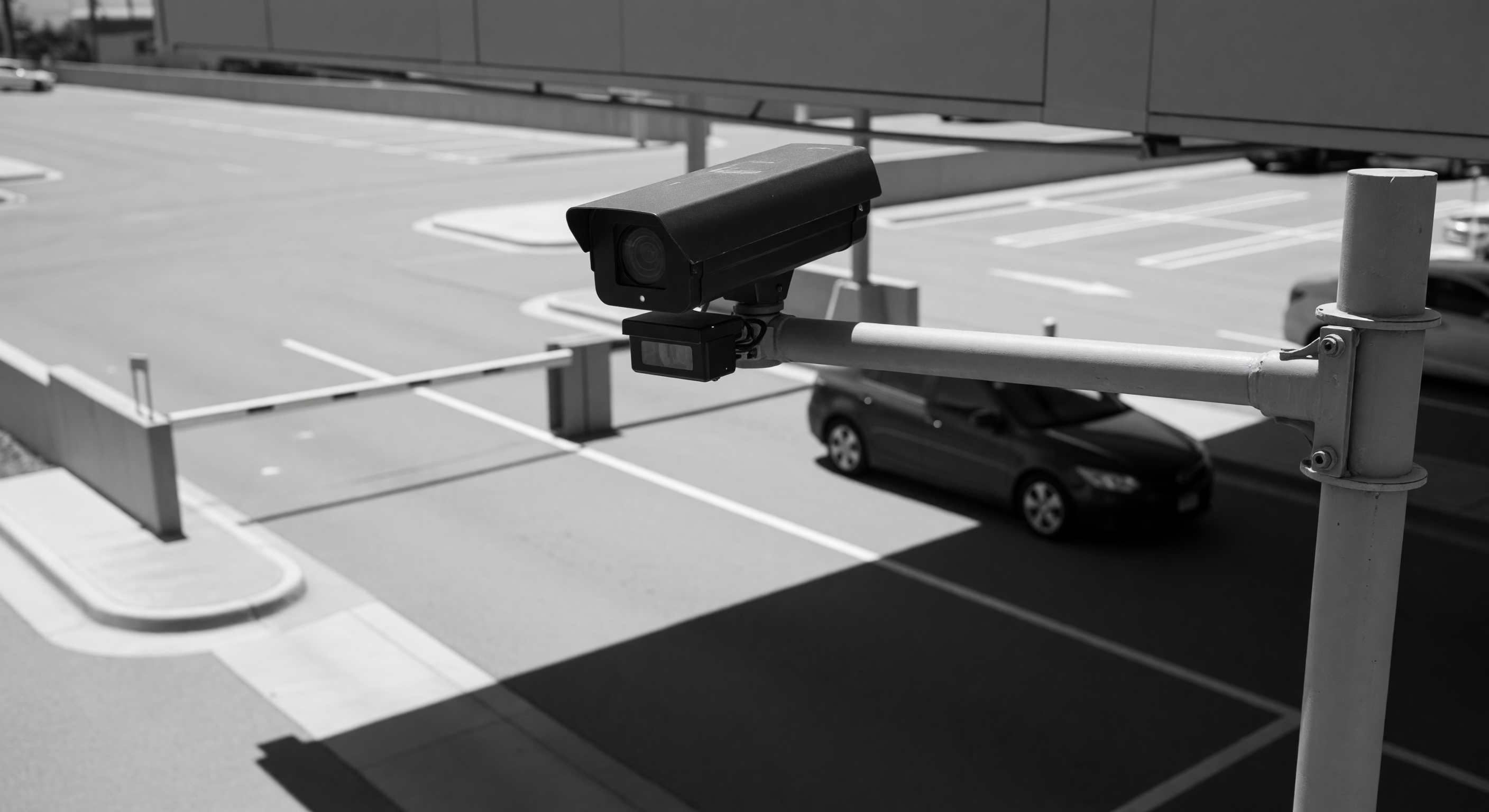 Two vehicles closely following through a parking lot barrier gate, demonstrating a tailgate event