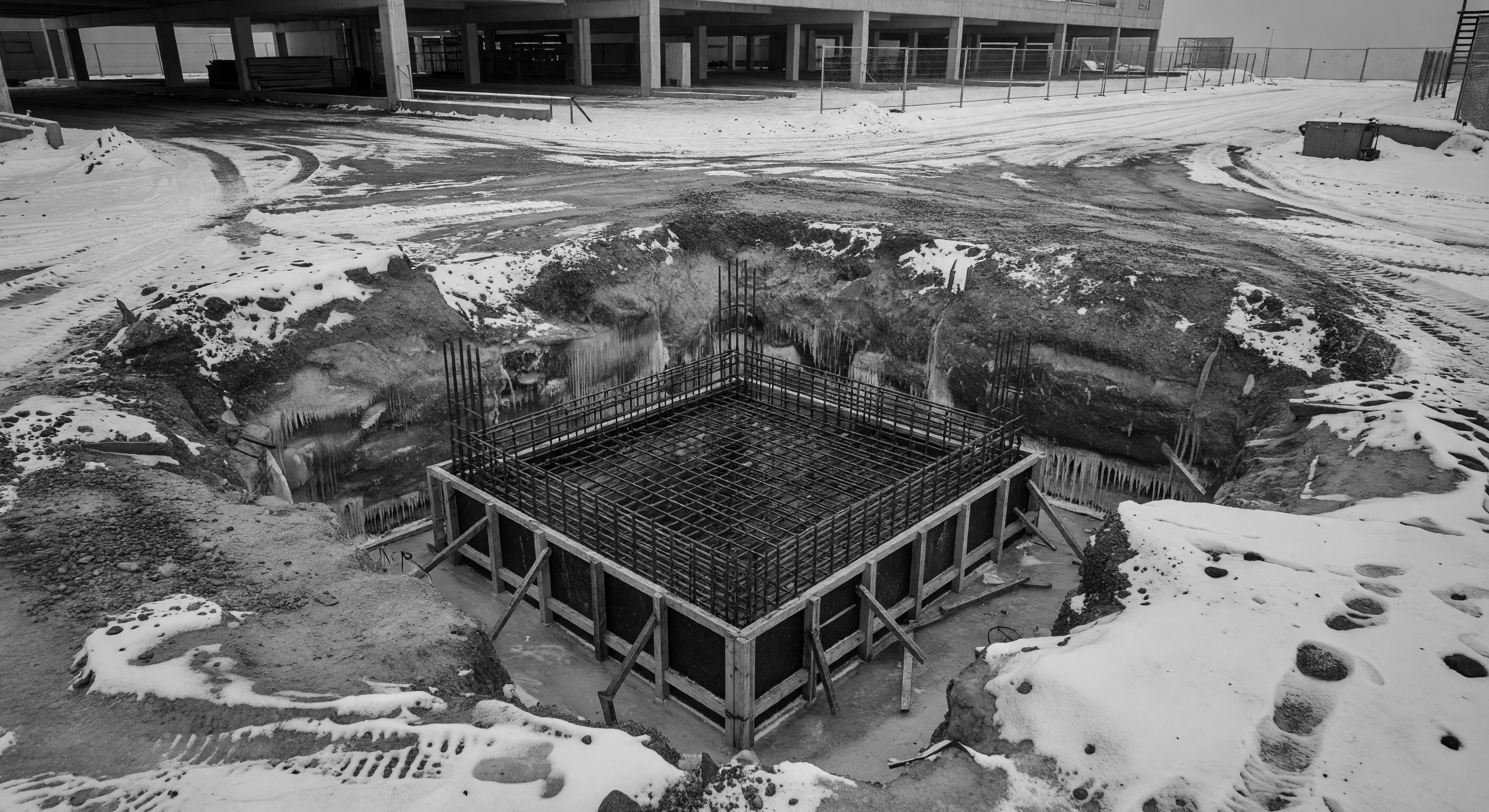 A parking barrier gate foundation excavated through frozen ground showing reinforced concrete footing below frost line