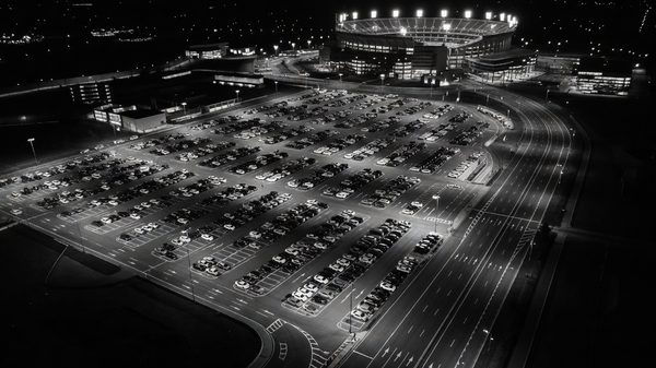 Wide view of a large surface parking lot beside a stadium under floodlights